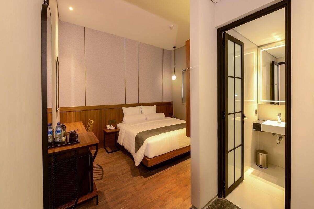 A hotel room with a bed, bedside table, and a bathroom with a sink and mirror.