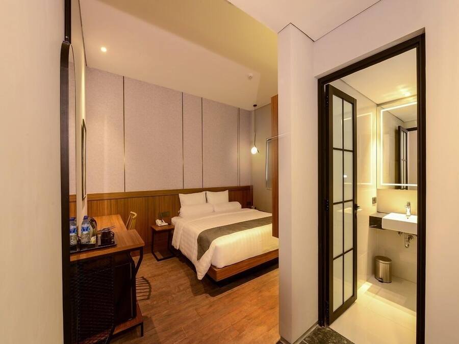 A hotel room with a bed, bedside table, and a bathroom with a sink and mirror.
