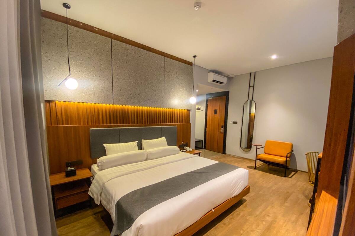A modern hotel room with a large bed, bedside tables, a chair, and a mirror.