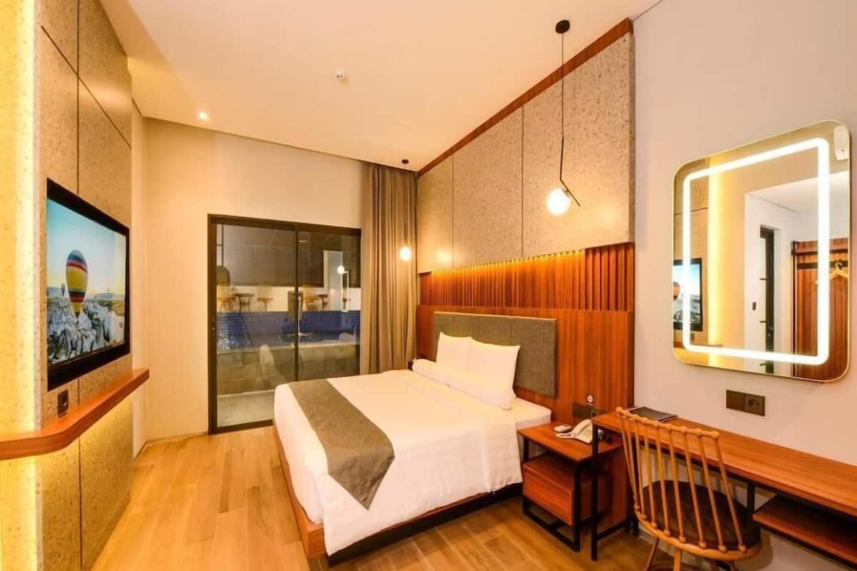 A hotel room with a bed, a desk, a chair, a TV, and a large mirror.