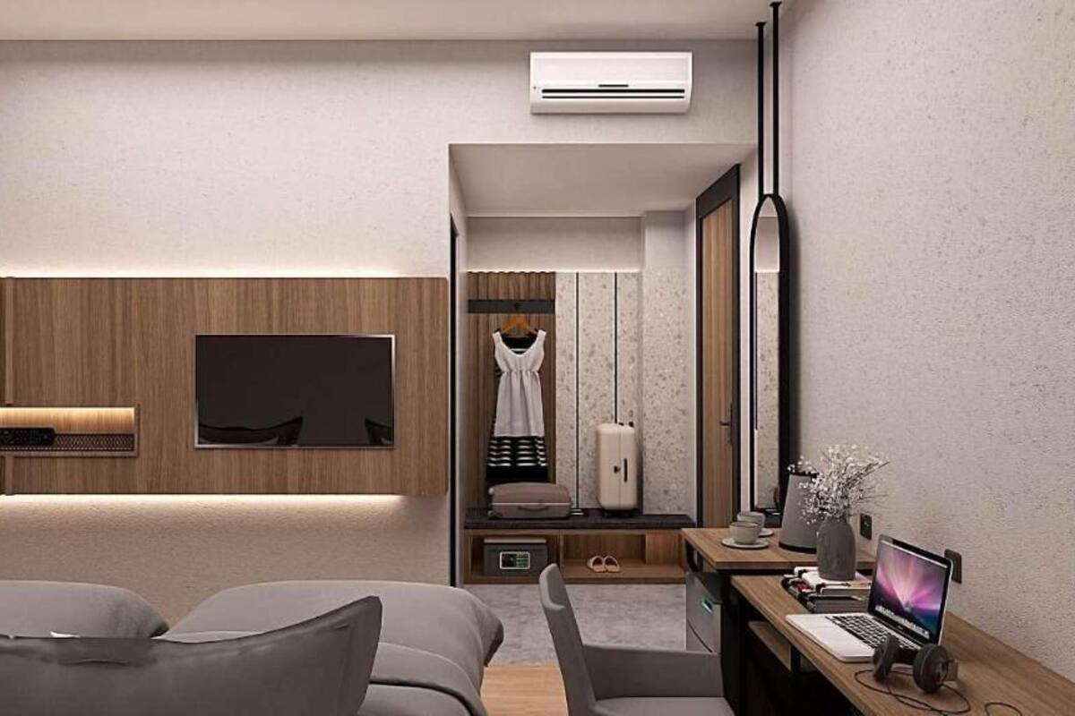 A modern hotel room with a flat-screen TV, a desk with a laptop, a chair, a sofa, and a wardrobe.