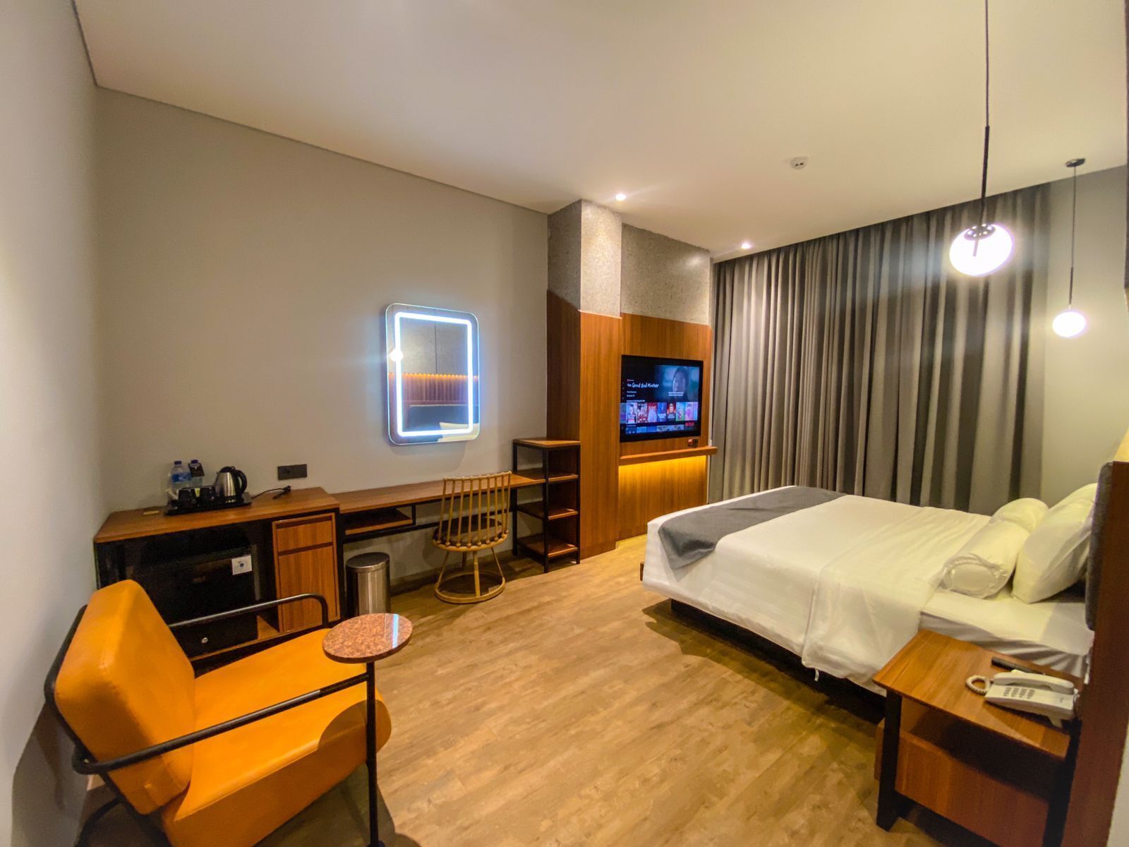 A hotel room with a bed, a desk with a chair, a TV, and a minibar.