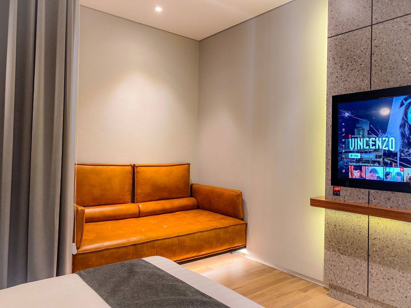 A modern living room with a leather sofa, a flat-screen TV mounted on a wall, and a wooden floor.