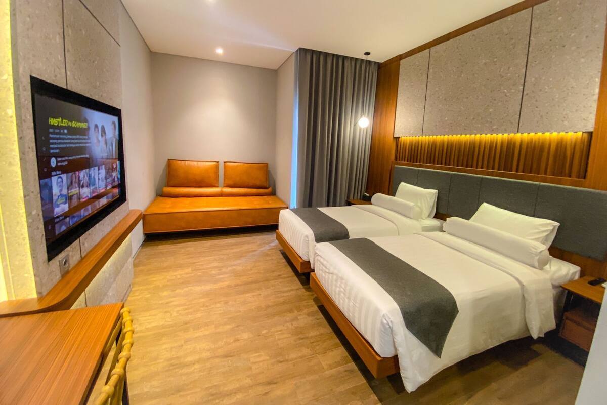 A modern hotel room with a large bed, a sofa, a TV, and a wooden floor.