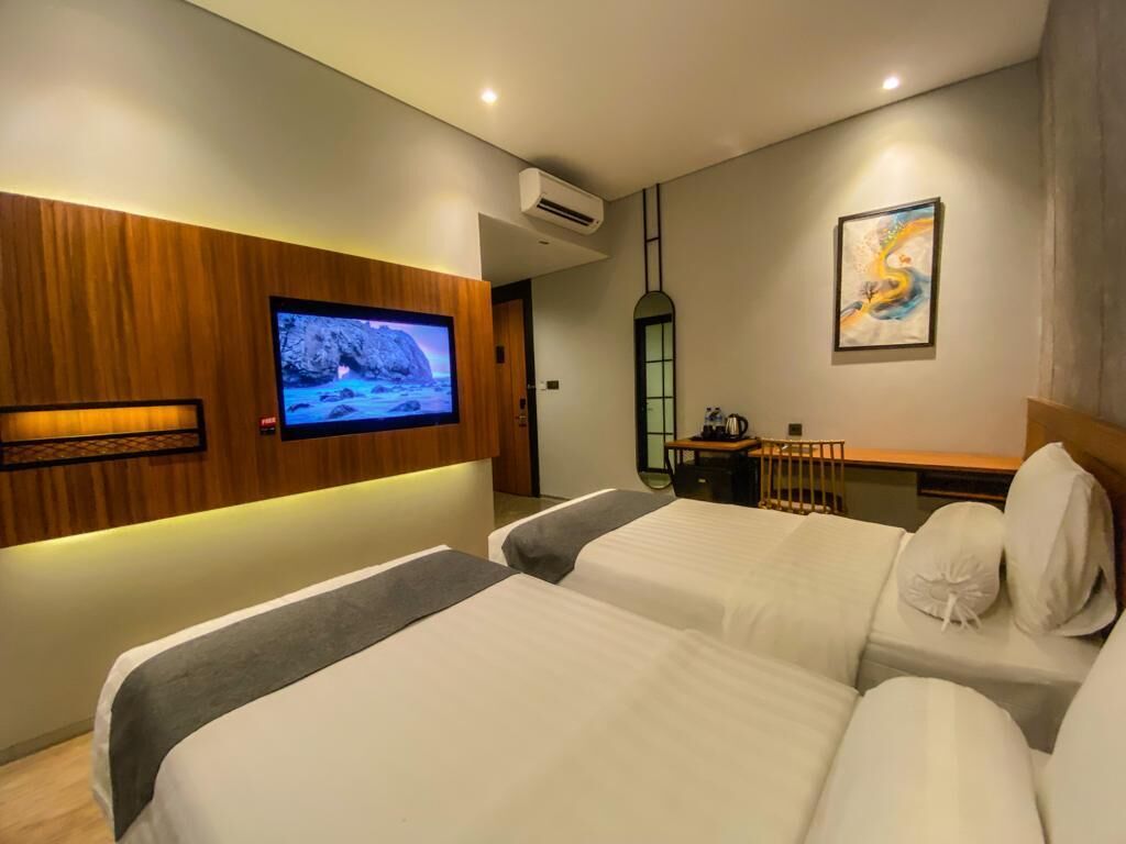 A hotel room with two beds, a TV mounted on a wooden panel, a desk with a chair, and a painting on the wall.