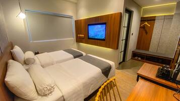 Habitación de hotel con dos camas, un televisor montado en la pared, un escritorio de madera y un banco.