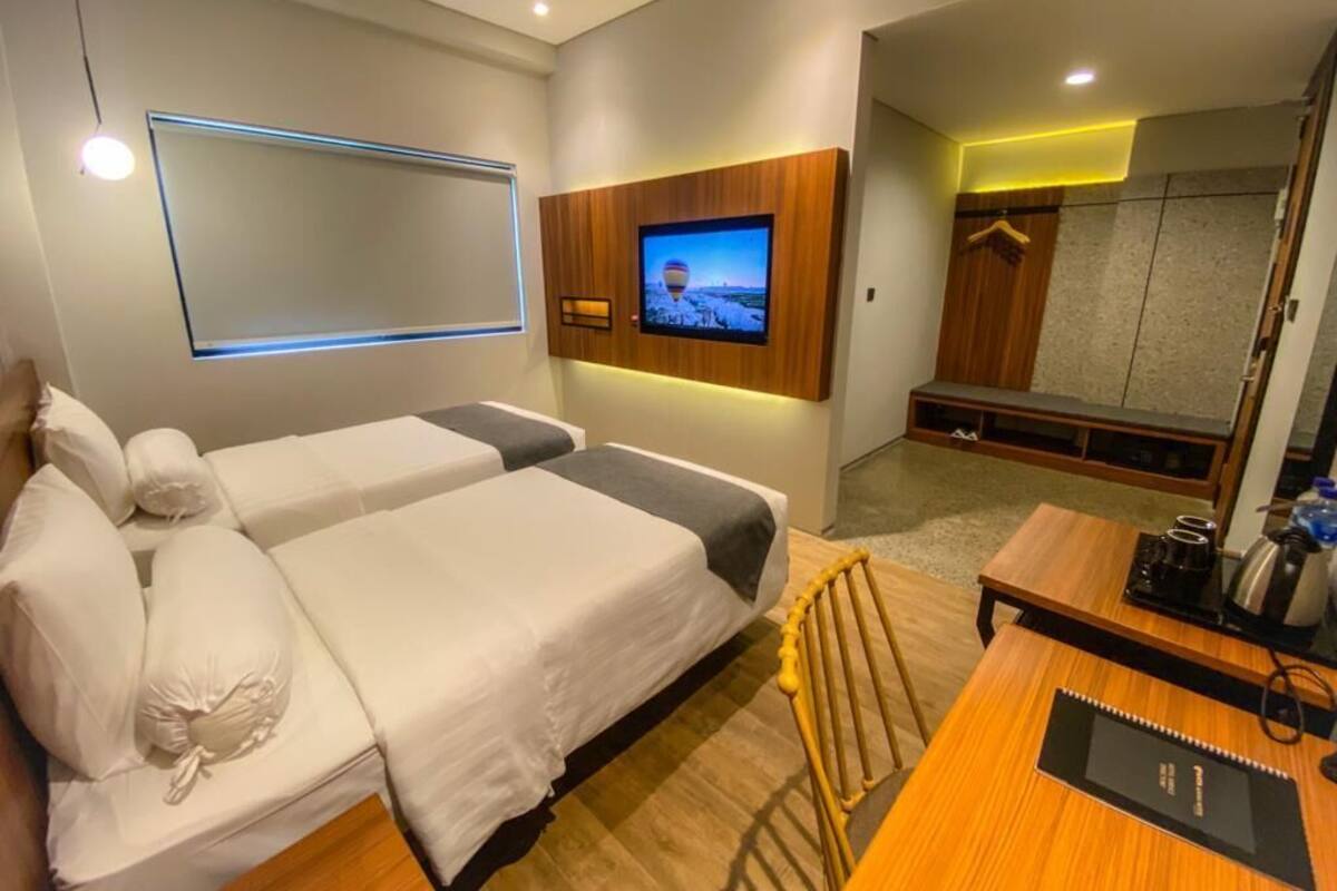 A hotel room with two beds, a TV mounted on the wall, a desk with a chair, and a mirror.