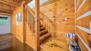 Ein Holzinnenraum mit einer Treppe zu einer zweiten Etage, einem Korb mit einer Schüssel und einer zur Außenwelt führenden Tür.