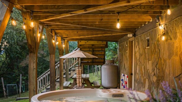 Ein Whirlpool unter einer Hollaube mit Lichterketten, umgeben von einer rustikalen Holzhütte und einem Picknickbereich.