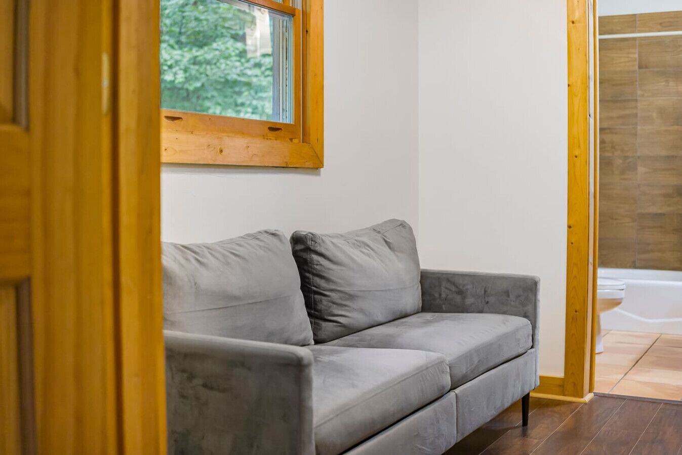 Un sofá gris en una habitación con un marco de puerta de madera y una ventana.