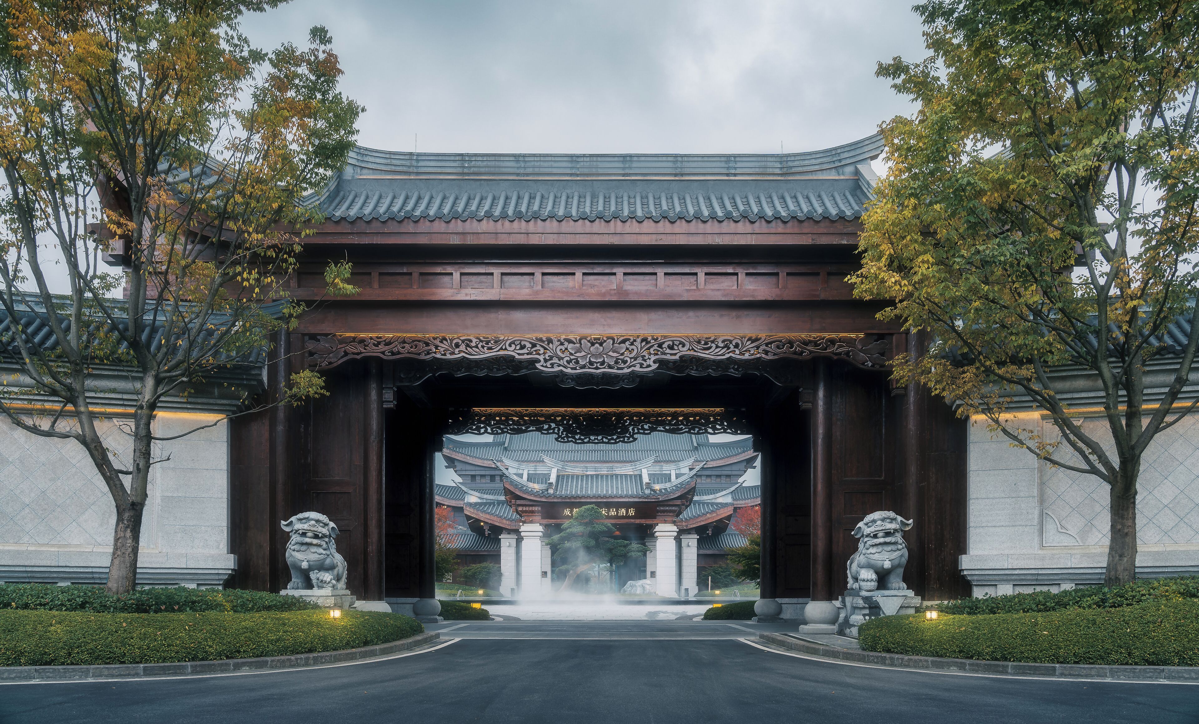 A traditional Chinese gate with intricate carvings, a stone lion statue, and a water fountain in the center.