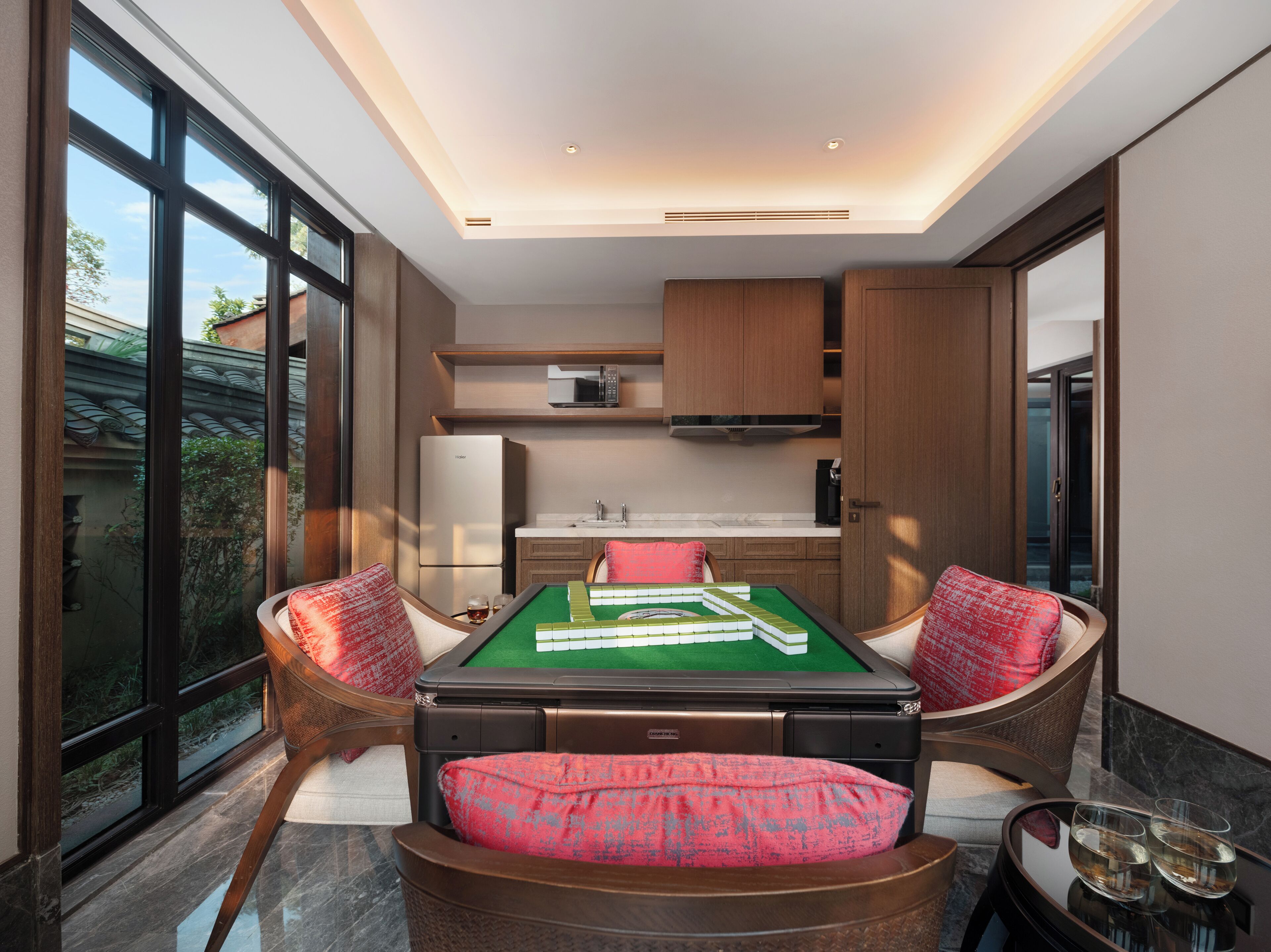 Una habitación moderna con mesa de billar, dos sillones mullidos, zona de cocina y ventanas amplias.