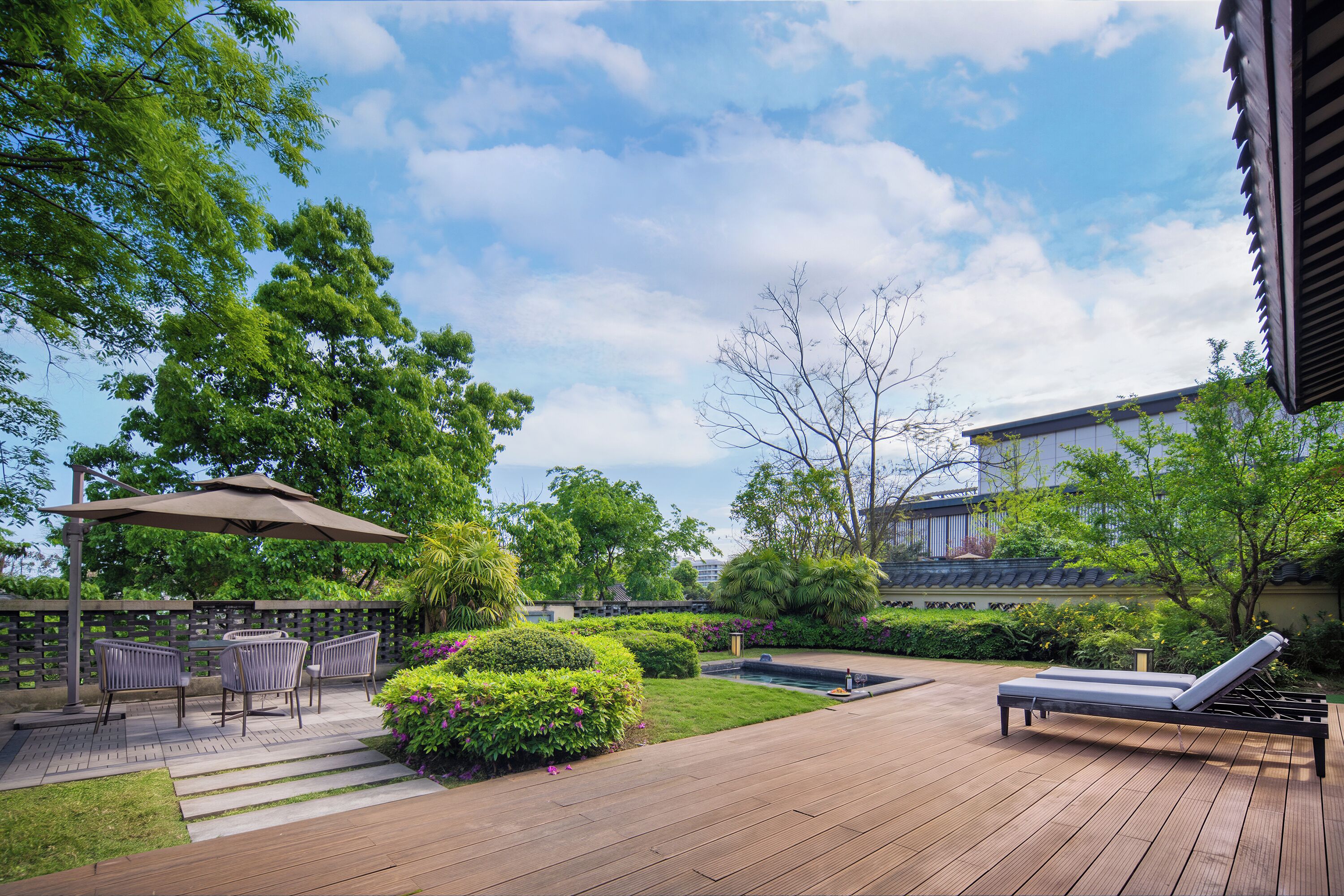 A wooden deck with outdoor furniture, a small water feature, and lush greenery.