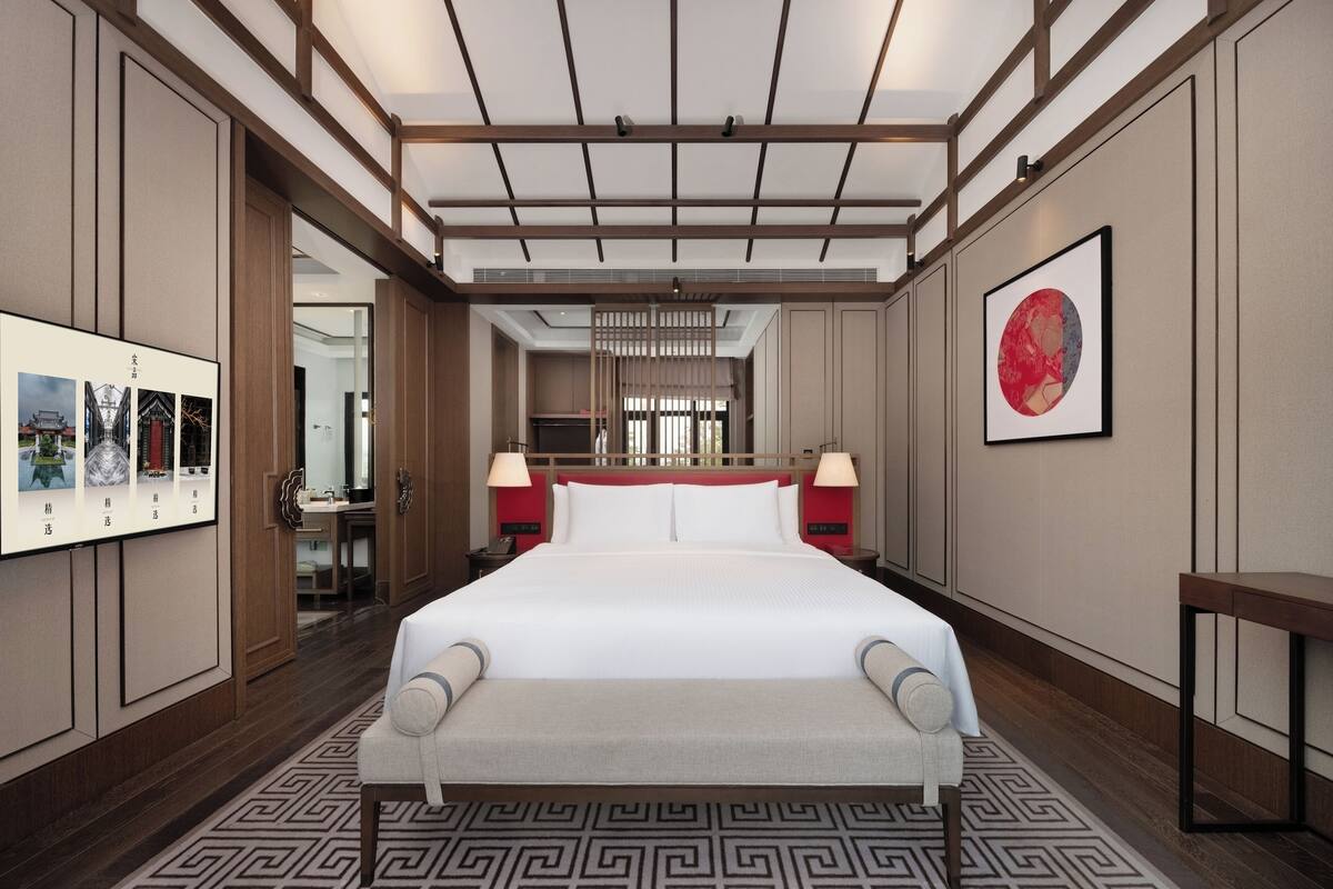 Una camera d'albergo moderna con un letto grande, una scrivania e una sedia. Si nota un'ampia finestra e un quadro appeso al muro.