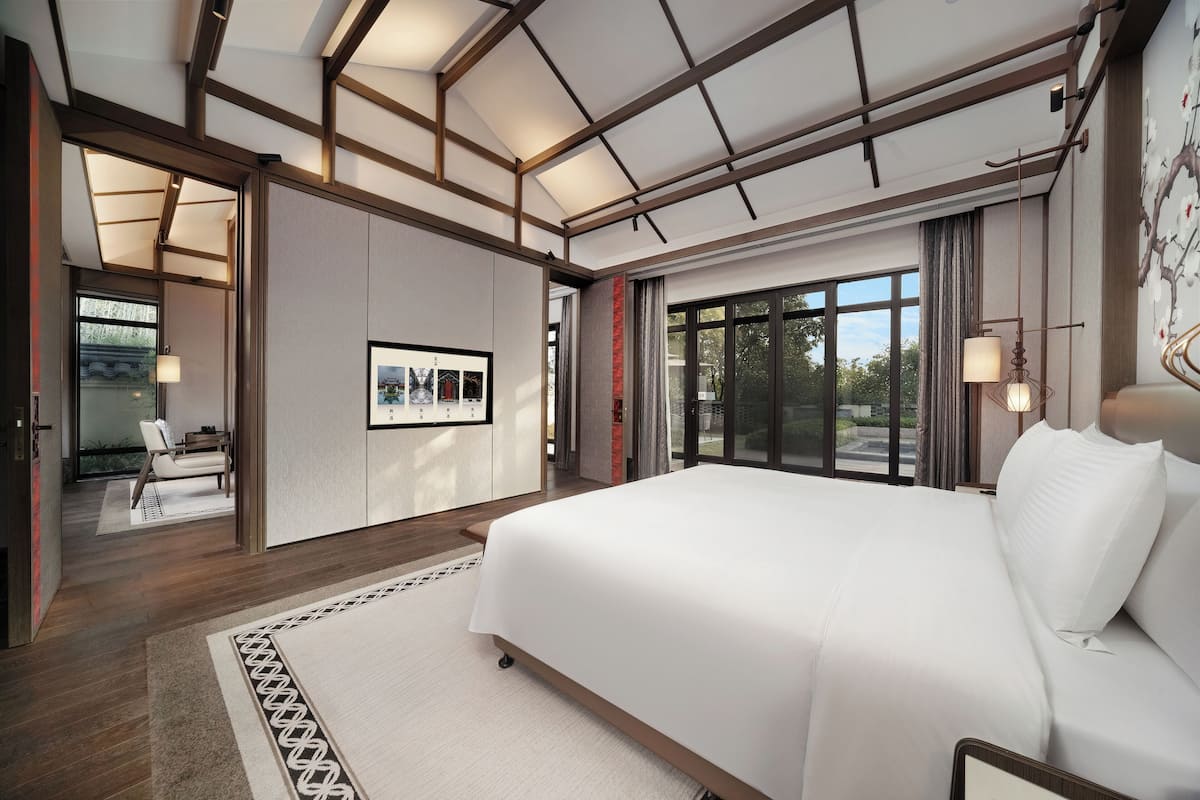 Camera d'albergo moderna con un letto grande, vista sull'esterno e un'area salotto separata con una sedia e un tavolo.