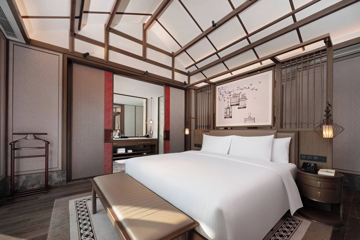 Una camera d'hotel moderna con un letto grande, una panca, una toeletta con uno specchio e un'opera d'arte appesa al muro.
