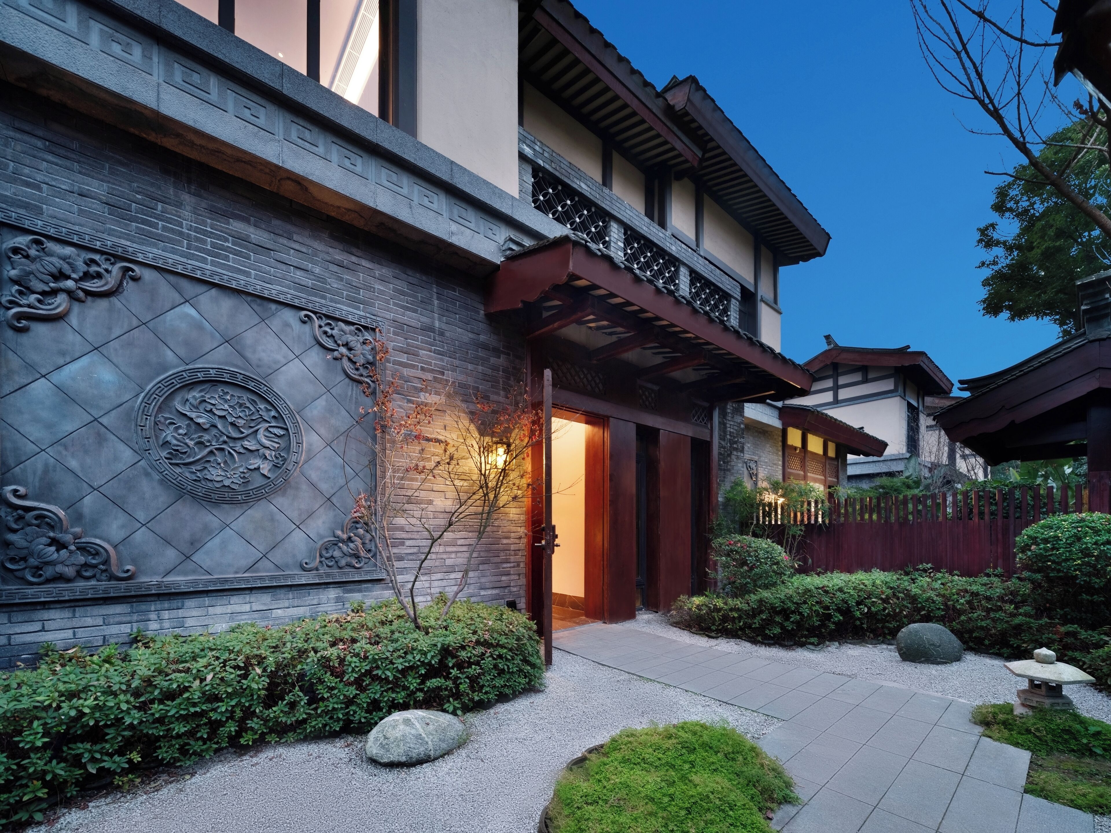 A traditional building with intricate wall carvings and a well-maintained garden with rocks and shrubs.
