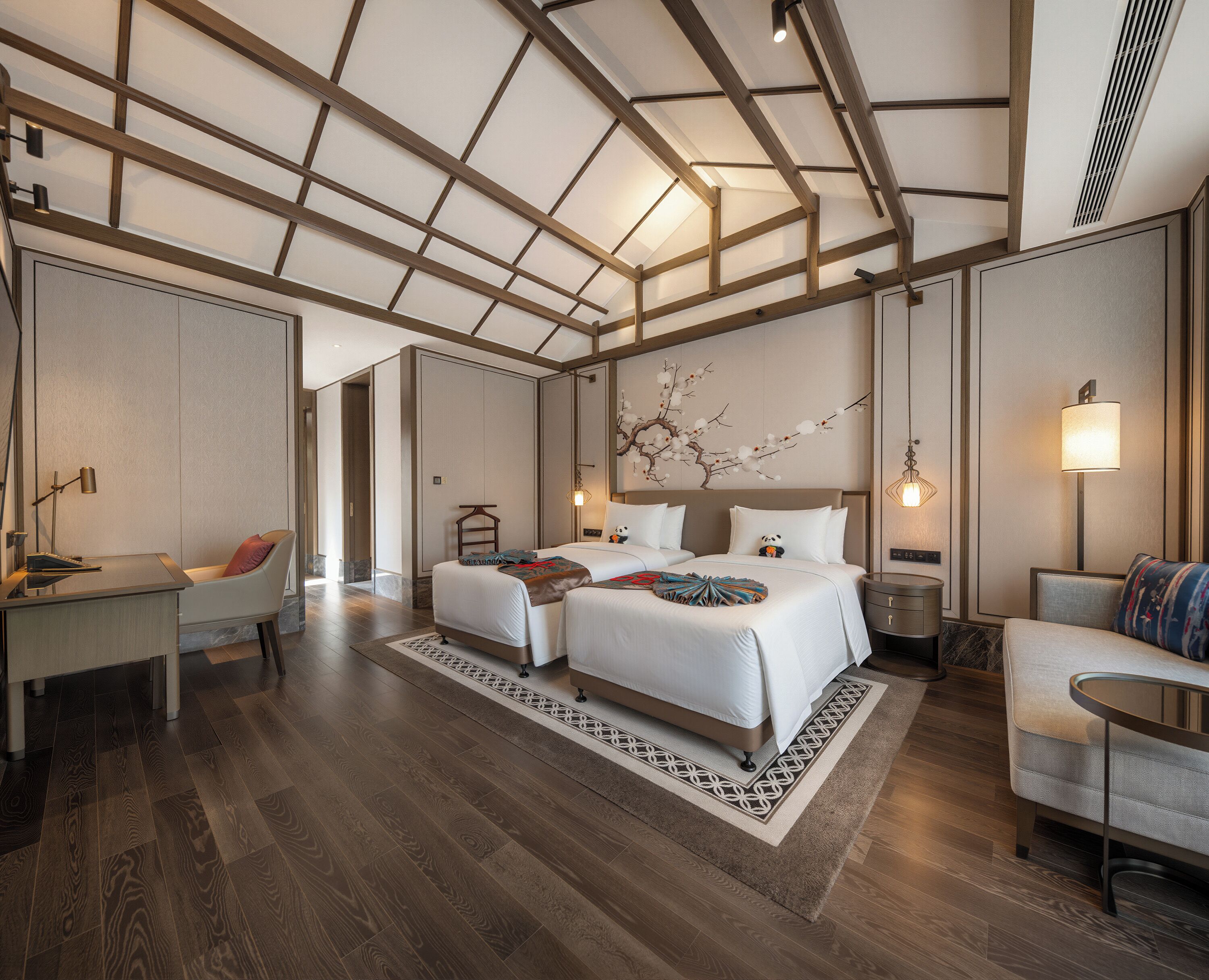 A hotel room with a large bed, a desk, a chair, a sofa, and a decorative wall piece.