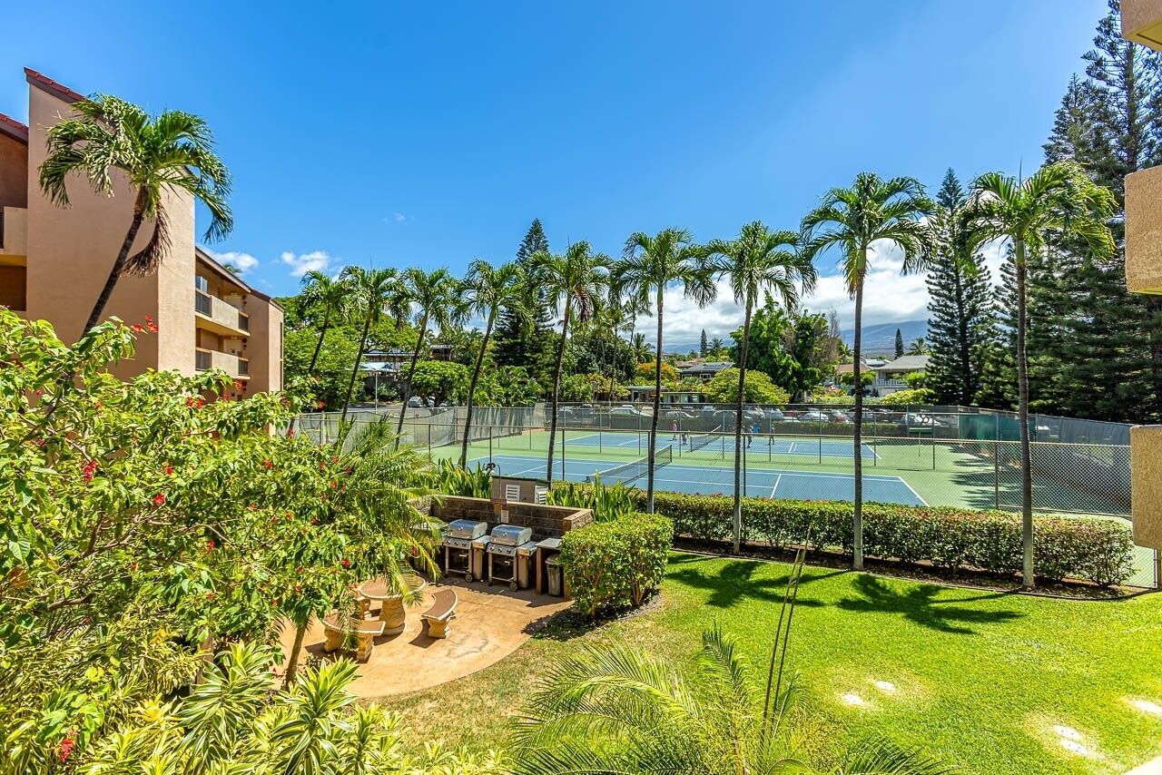 A tennis court surrounded by lush greenery and a building with balconies.