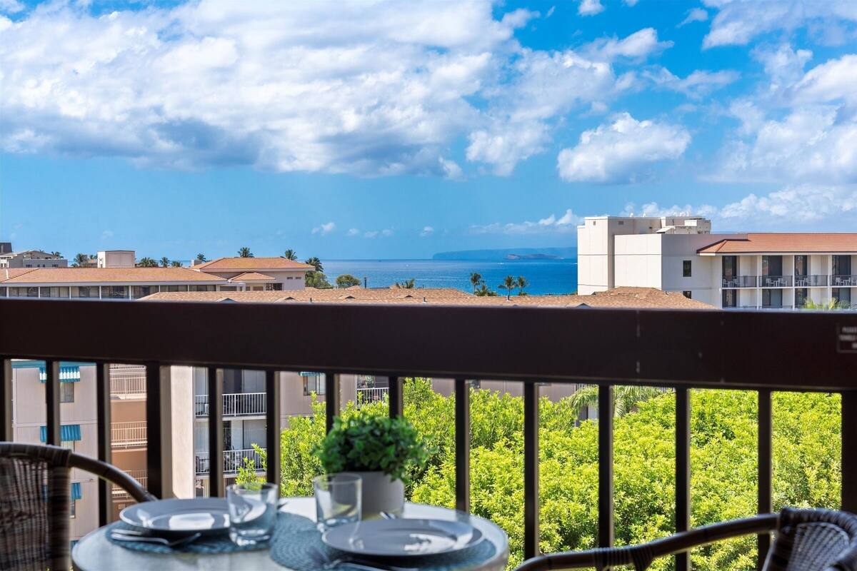 Ein Balkon mit Esstisch, der Blick auf die Küste mit Gebäuden und Grünflächen bietet.