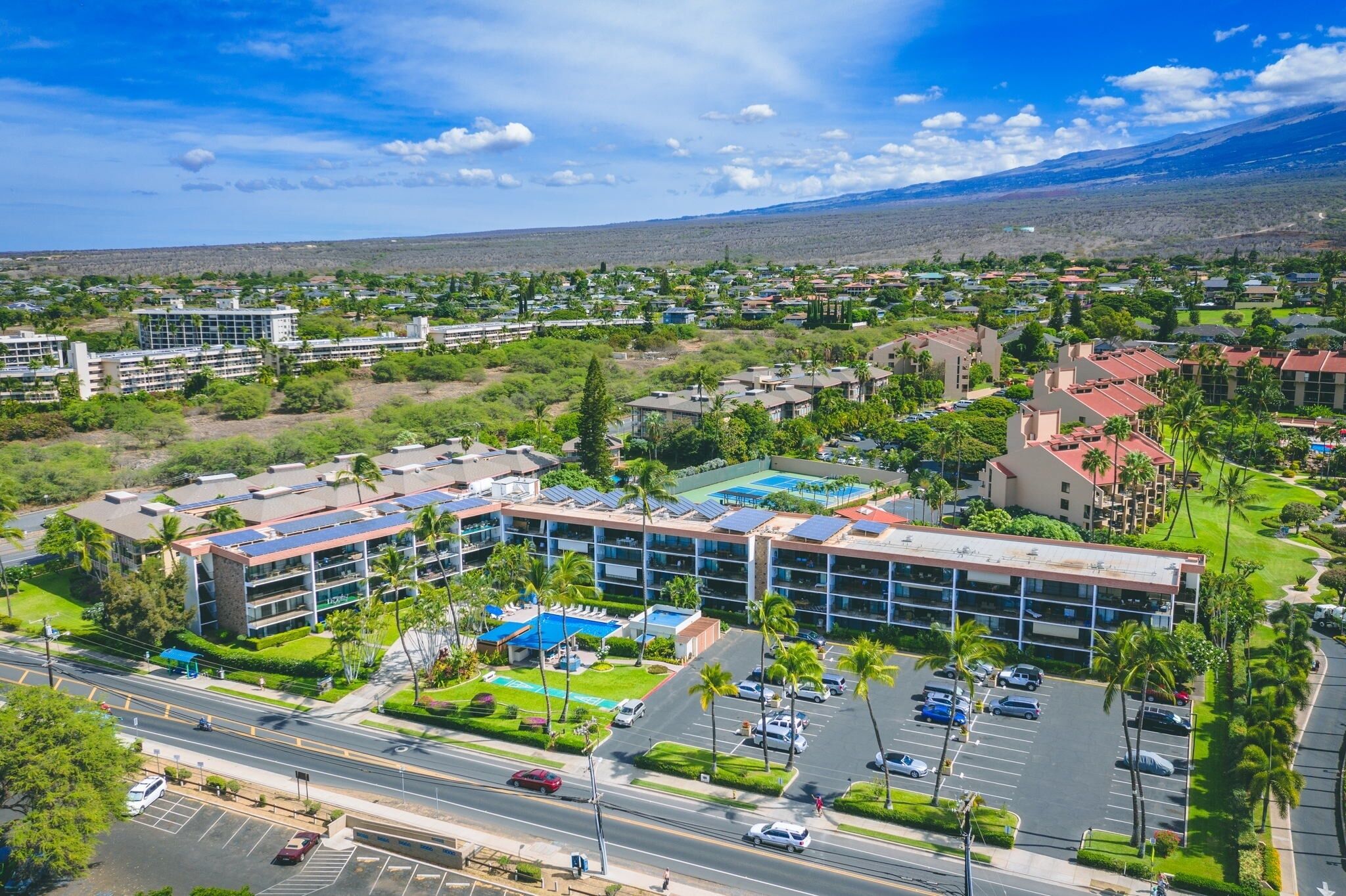 A multi-story hotel with a parking lot, surrounded by greenery and a mountainous backdrop.