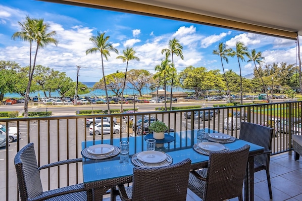 Ein Balkon mit Esstisch, der auf einen Parkplatz mit Autos und Palmen und den Blick auf das Meer blickt.