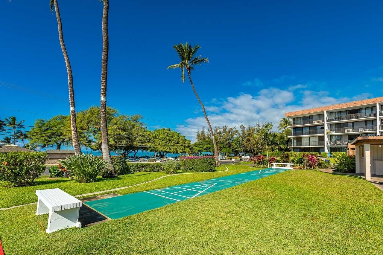 A courtyard with a shuffleboard court, palm trees, and a building with balconies.