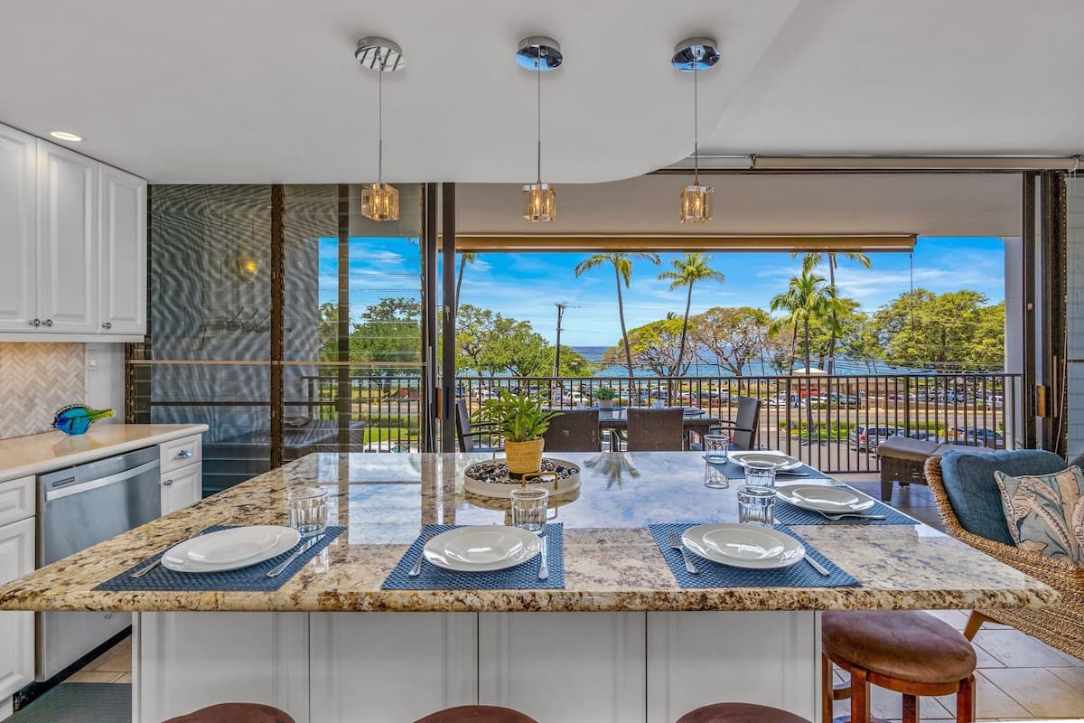A modern kitchen with a large island, white cabinetry, and a view of the outdoors.