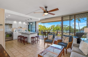 A modern kitchen with a central island, bar stools, and a dining area with wicker furniture.