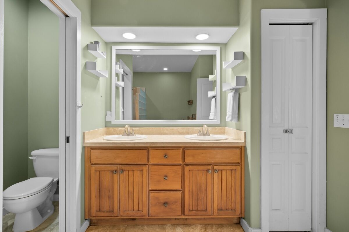 A bathroom with a wooden vanity, two sinks, a large mirror, and a white door.
