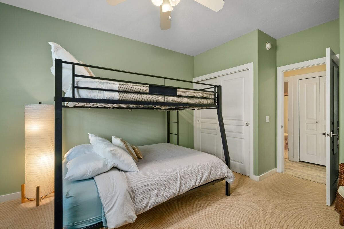 A bunk bed in a room with green walls, a ceiling fan, and a door leading to another room.