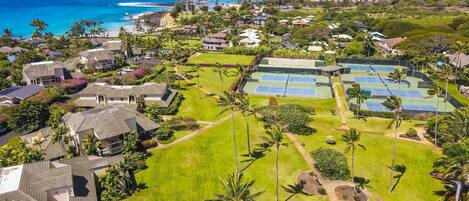 An aerial view of a residential area with houses, a tennis court, and a view of the ocean.