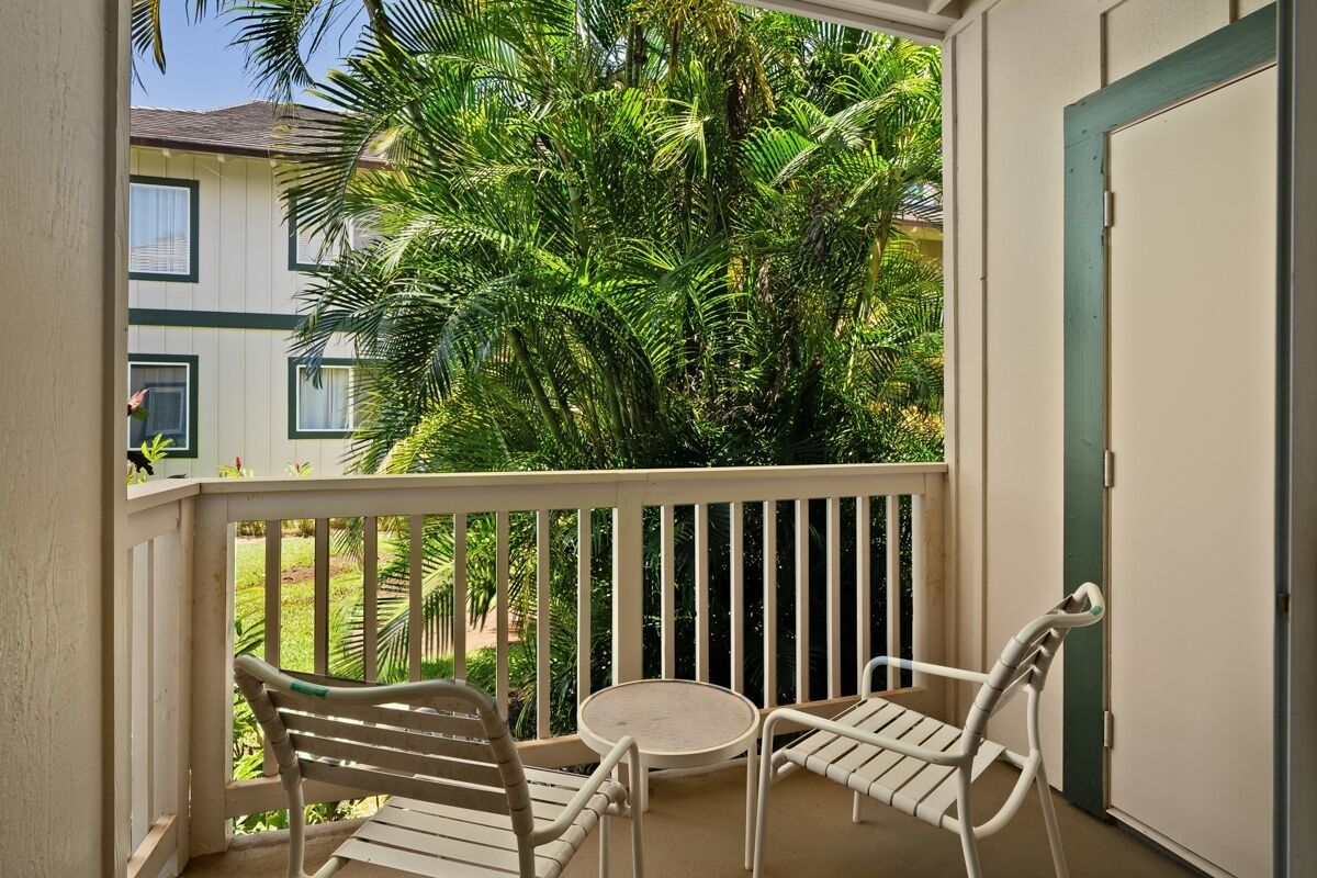 A balcony with two white chairs and a small round table, surrounded by a white railing.