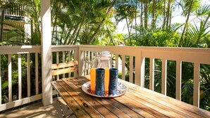 A wooden table with a glass pitcher and two blue tumblers on a plate, set on a balcony with white railings and lush green foliage in the background. - Kauai Regency at Poipu Kai by Coldwell Banker Island Rentals (Koloa)