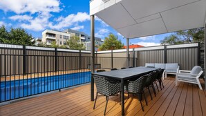 A wooden deck with a pool, outdoor seating, and a covered area.