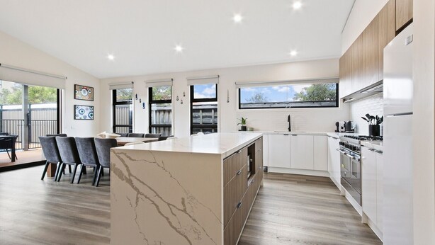 A modern kitchen with a marble island, wooden cabinets, and a dining area with chairs.