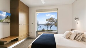 Une chambre à coucher comprenant un lit, un téléviseur fixé au mur, une armoire et une fenêtre donnant sur un lac et des arbres.