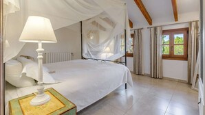 Ein Schlafzimmer mit Himmelbett, Nachttisch mit Lampe und Fenster mit Vorhängen.