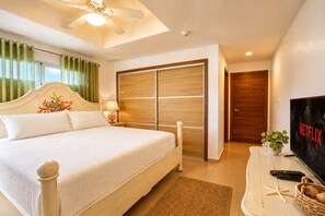 A hotel room with a bed, a TV, a ceiling fan, a wooden wardrobe, and a door.