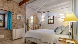 Ein Schlafzimmer mit einem Himmelbett, einem Nachttisch mit Lampe, einem Fenster mit Vorhängen und einem Heizkörper.