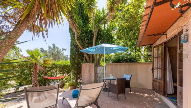 Eine Terrasse mit zwei Metallstühlen, einem Tisch und einem blauen Sonnenschirm.