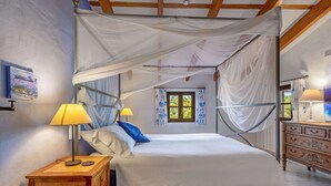 Ett sovrum med en himmelssäng, två sänglampor, ett träbord vid sängen, en byrå och ett fönster med gardiner.