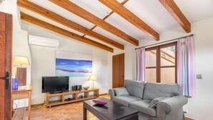 A living room with a grey sofa, wooden beams, a TV, and a painting.