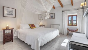 A bedroom with a large bed, a bedside table, a chair, a window with curtains, and a radiator.