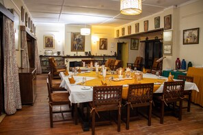 Un espace repas avec une longue table dressée pour accueillir plusieurs personnes, des chaises en bois et une variété d’articles de table.