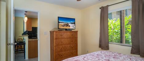 Un dormitorio con cama, cómoda, ventilador de techo, ventana con cortinas y vista a zonas verdes.