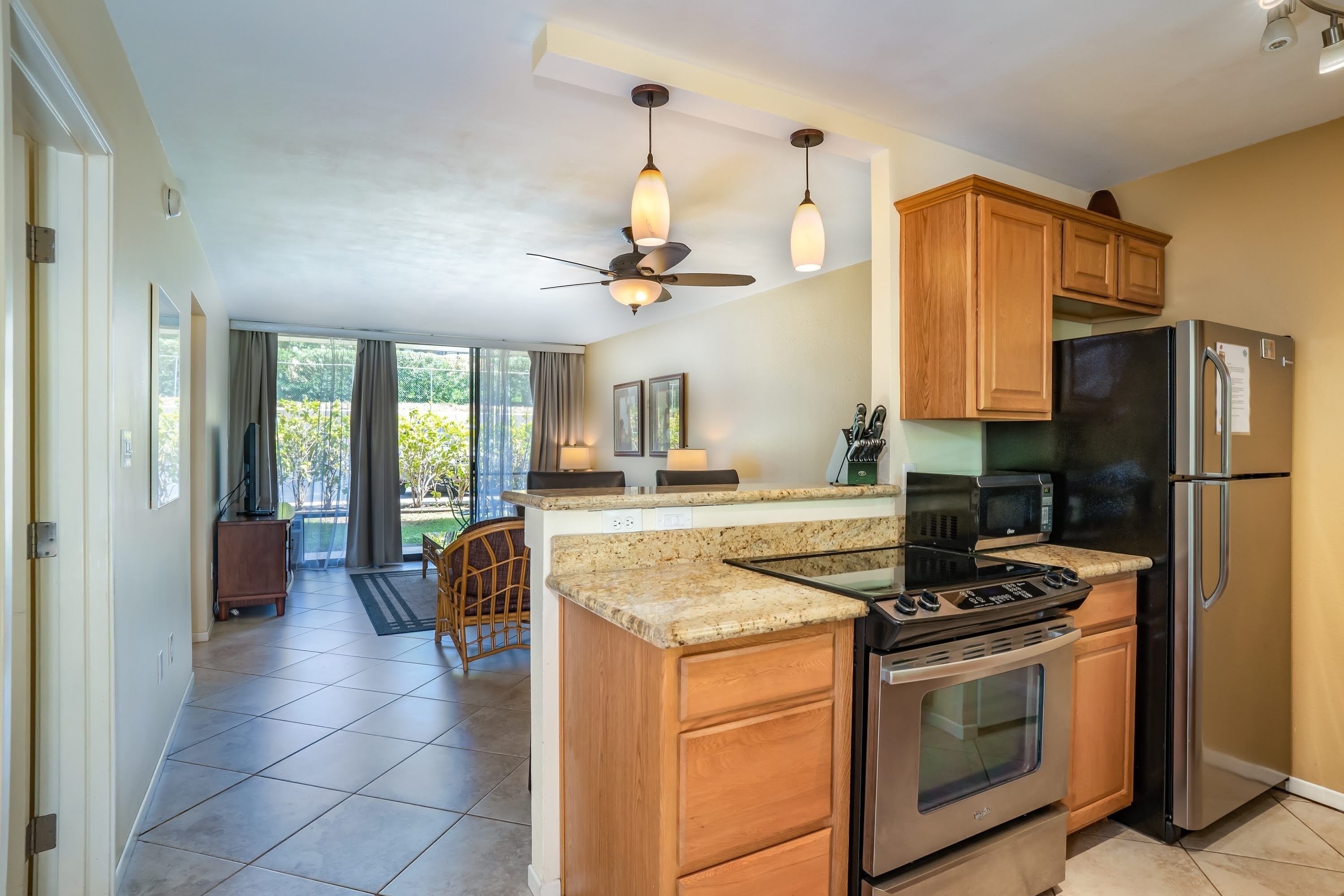 A modern kitchen with wooden cabinets, a stainless steel refrigerator, a built-in oven, and a central island with a stove.