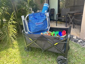 Ein fahrbarer Wagen mit einer blauen Tasche und verschiedenen Gegenständen, draußen auf einer Rasenfläche mit Palmen.
