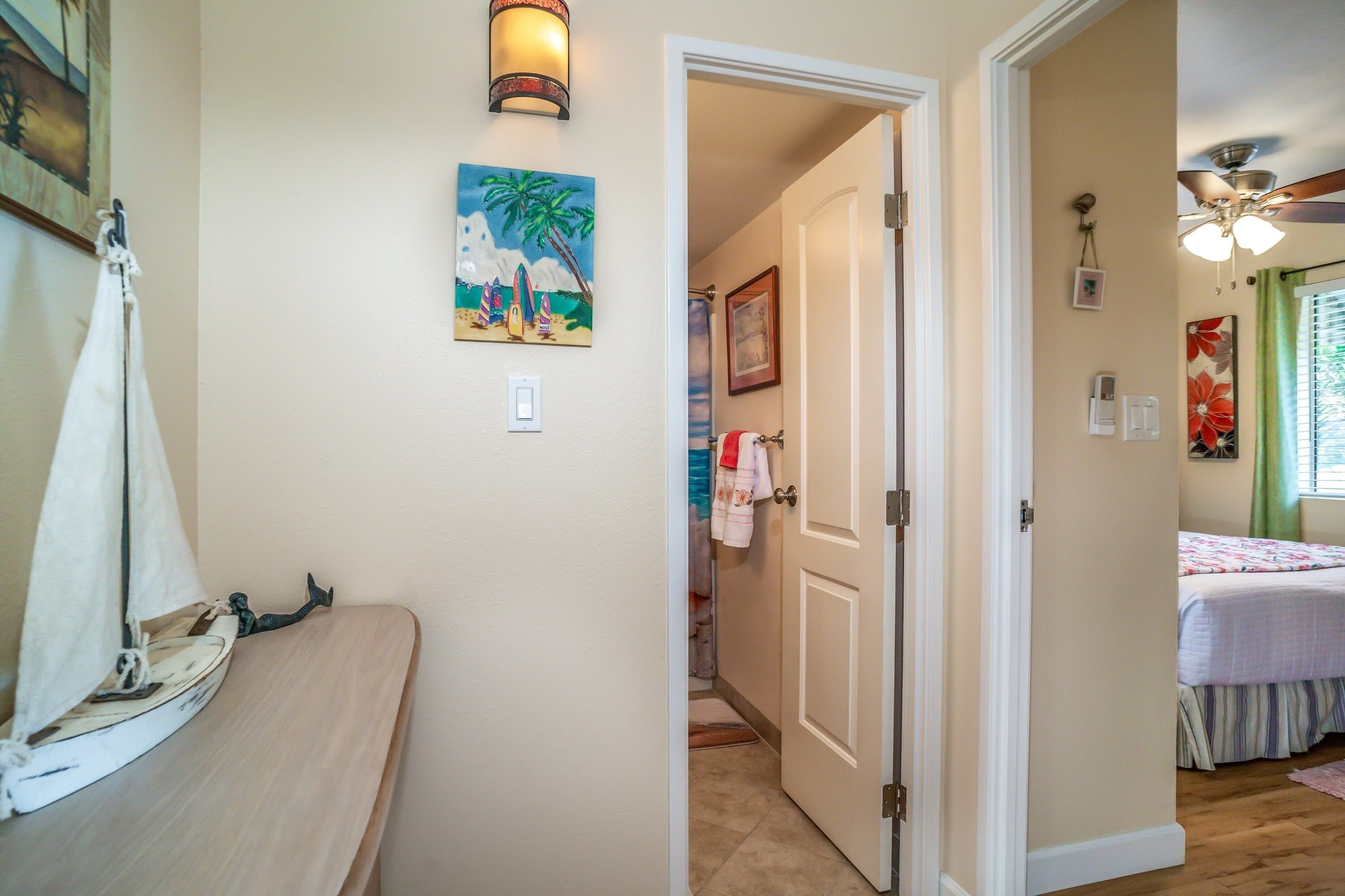 A bedroom with a bed, a ceiling fan, and a painting of a beach scene.