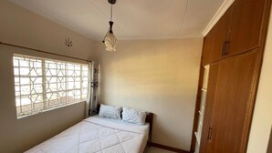 Un dormitorio con una cama, una ventana con diseño geométrico, una lámpara colgante y armarios de madera.